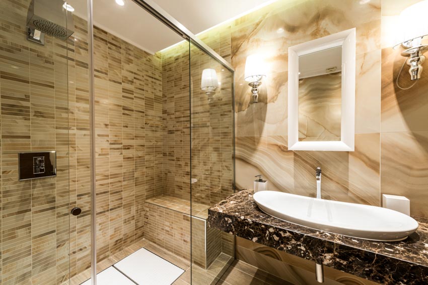 Bathroom with countertop, sink, mirror, wall mounted lights, and glass tile shower