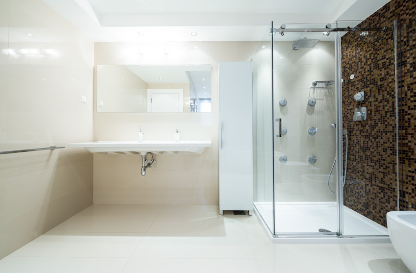 Bathroom with frameless mirror, brown accent tiles on the wall and white floor