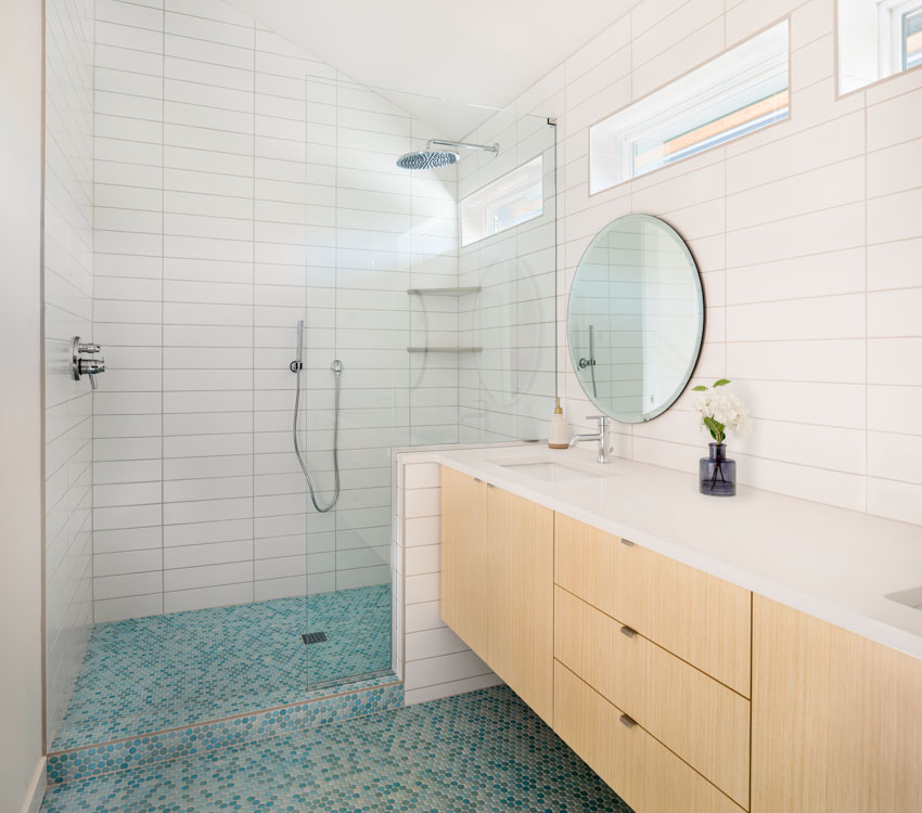 Bathroom with glass tile floor, subway tile wall, glass door, cabinets, countertop, sink, mirror, and windows