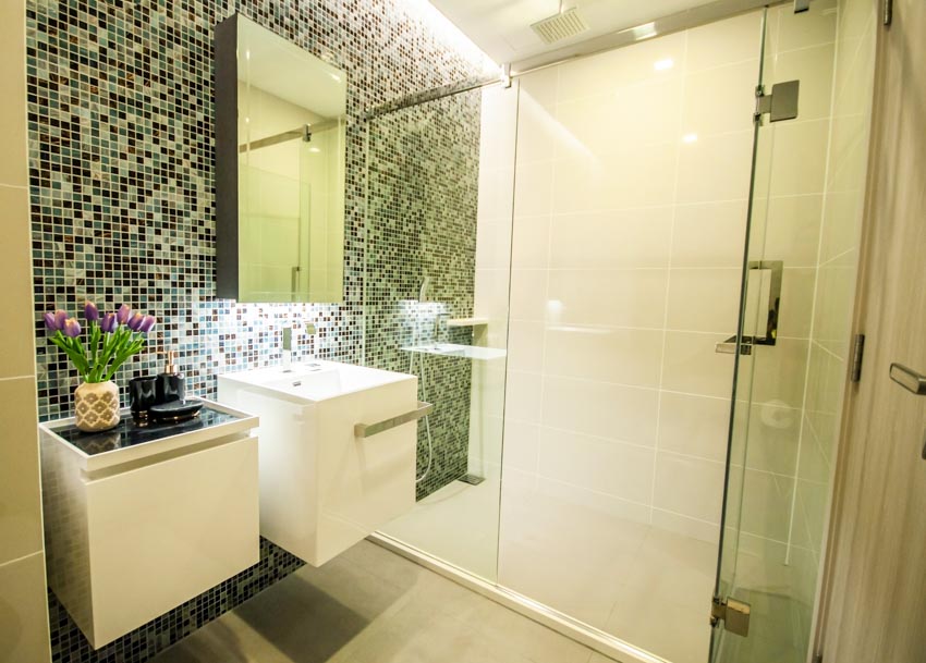 Bathroom with green glass mosaic tile shower, vanity area, glass door, sink, and mirror