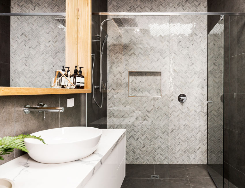 Bathroom with herringbone mosaic tile shower wall, countertop, sink, mirror, and glass divider