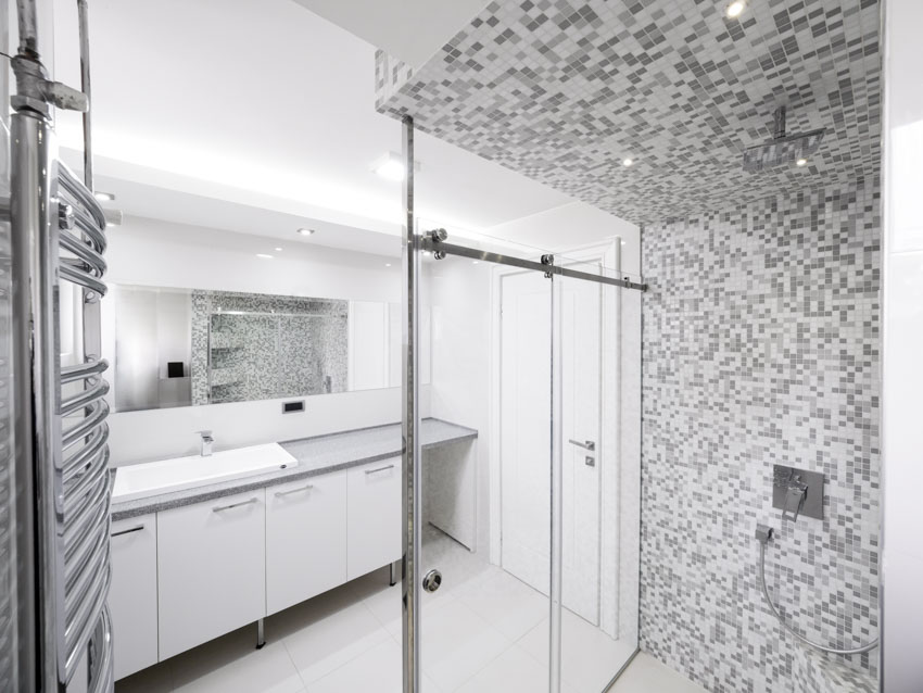 Bathroom with grey tiles, white door and glass walls with steel frame