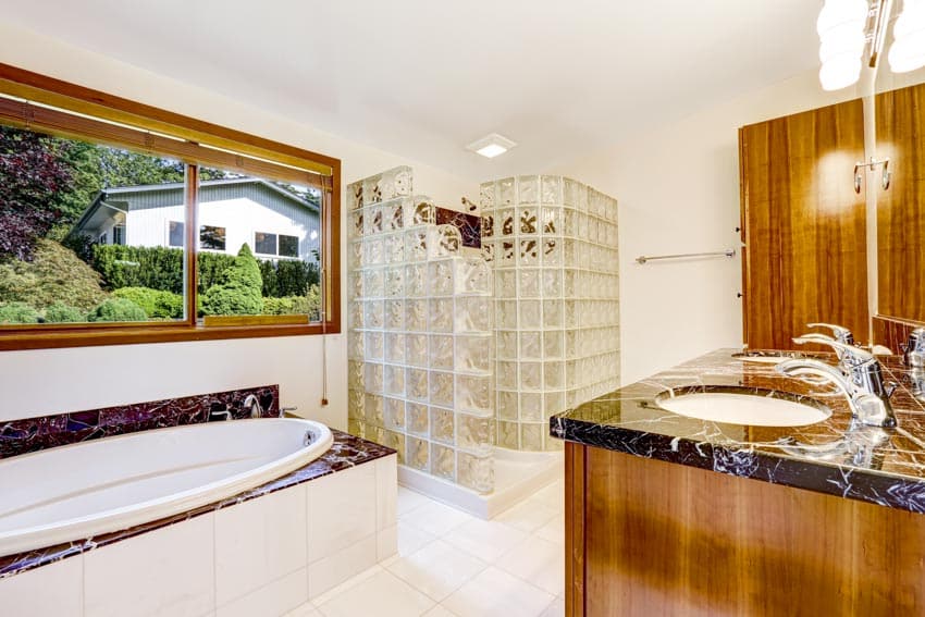 Bathroom with shower glass block enclosure, tub, countertop, sink, and window