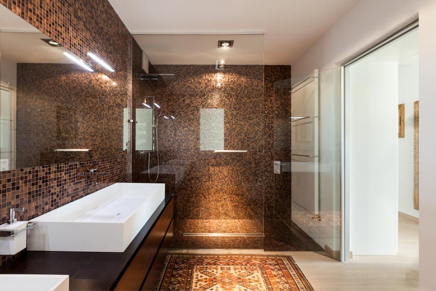 Beautiful bathroom with glass tile shower, glass door, floor rug, sink, countertop, mirror, and ceiling lights