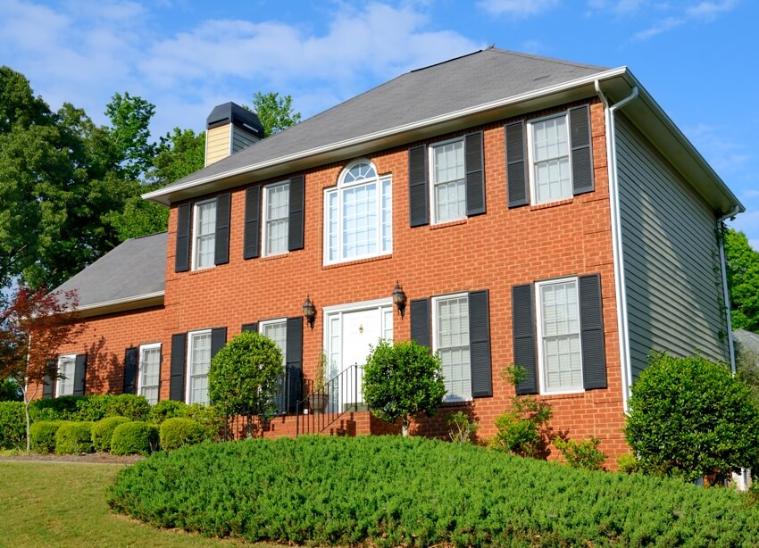 A beautiful brick home with gray shutters and beautifully landscaped front lawn