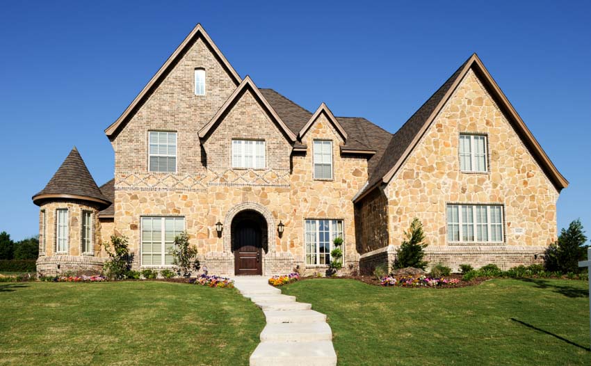 Beautiful house exterior with sandstone siding, walkway, lawn, windows, pitched roof, and front door