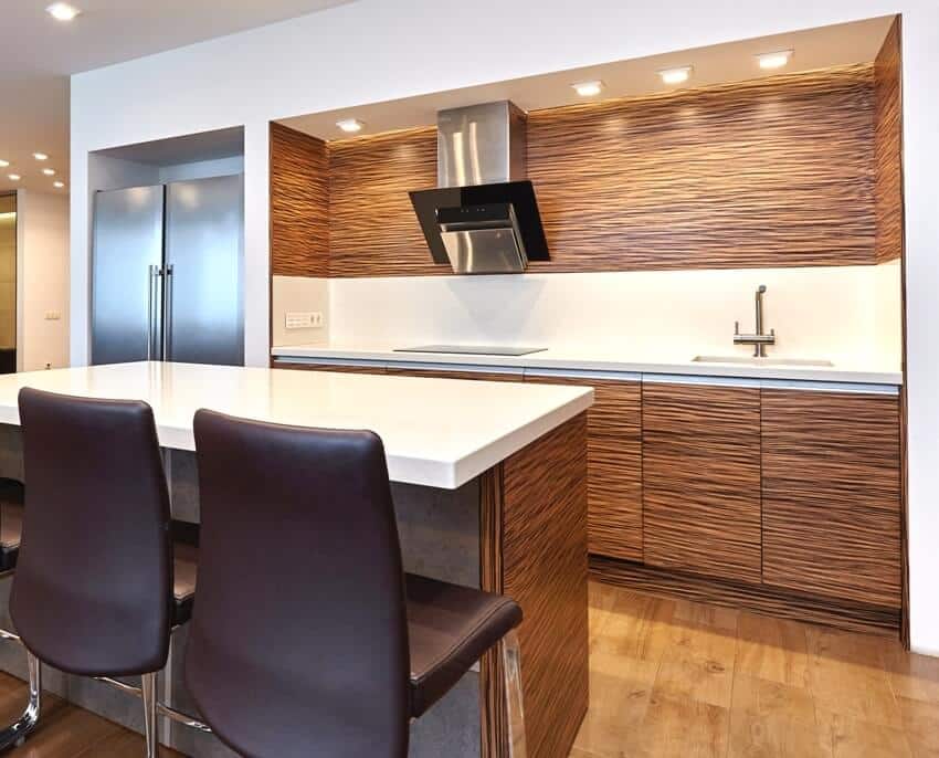 A beautiful kitchen interior with teak kitchen cabinets and island with quartz countertop and black chairs