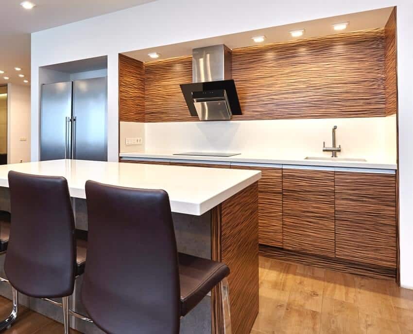 A beautiful kitchen interior with teak kitchen cabinets and island with quartz countertop and black chairs 