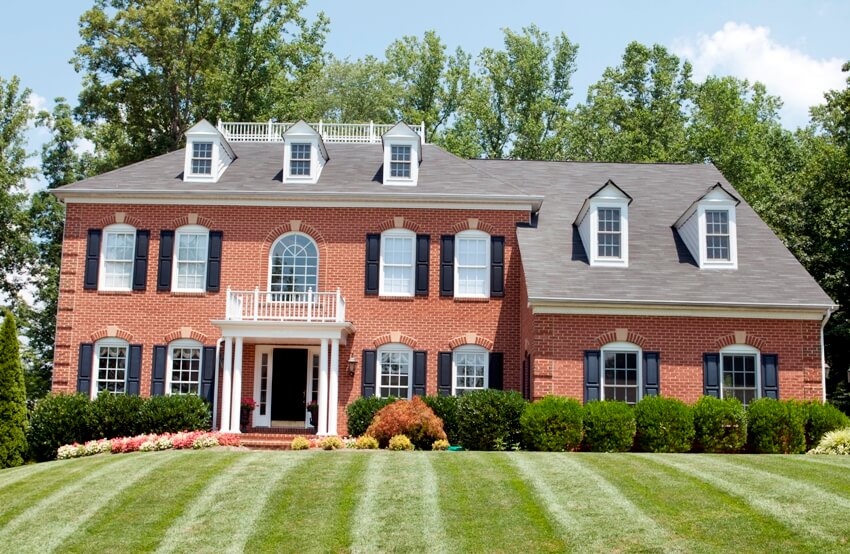 Beautiful large new American house in red brick with black shutters and lovely green lawn in summer