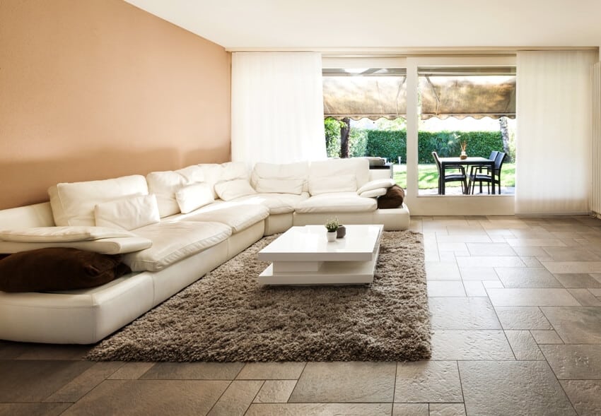 A beautiful living room with warm tones, white large sofa, tv and potted plants on white console and travertine flooring