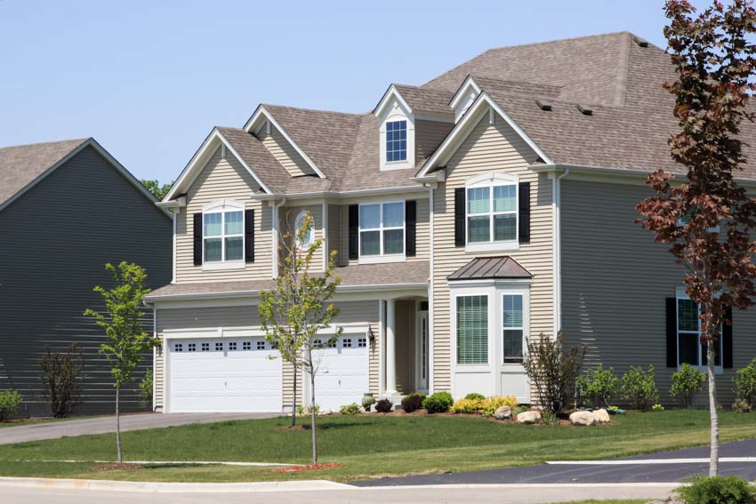 Beautiful tan house with window, shutters, garage, pitched roof, dormer, and front lawn