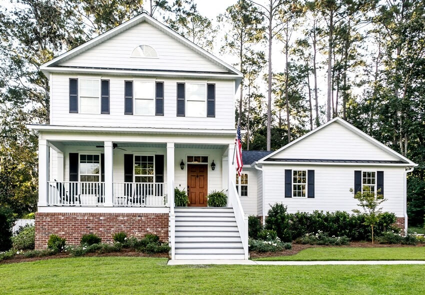 A beautiful white exterior farmhouse with traditional wood front door, window shutters, and stairs going up to the front entrance