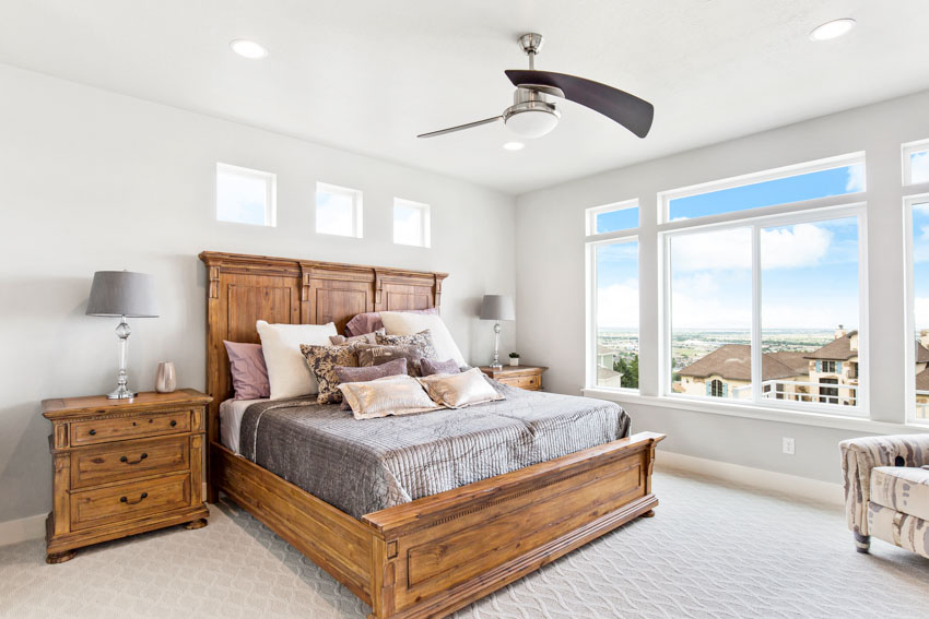 Bedroom with retractable ceiling fan, bed, headboard, pillows, nightstand, lamp, and windows