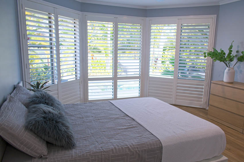 Bedroom with white window shutters, bed, pillows, and dresser table