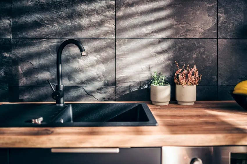 Kitchen with black stone backsplash, wood countertop, sink, and faucet
