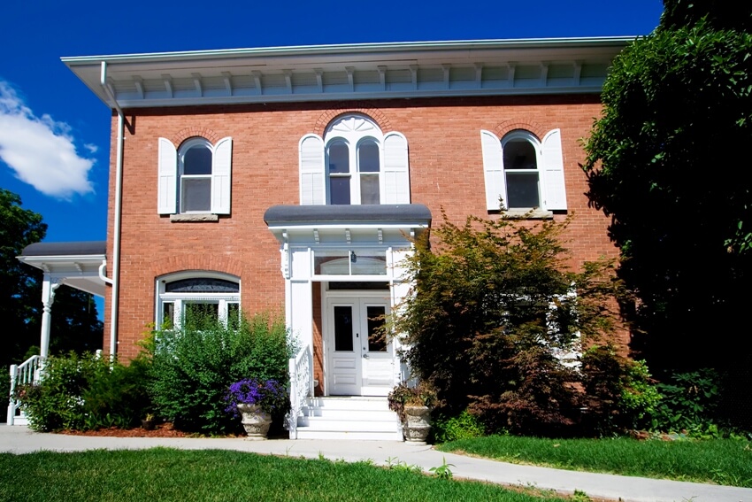 A classic old style brick house with white doors, windows and shutters