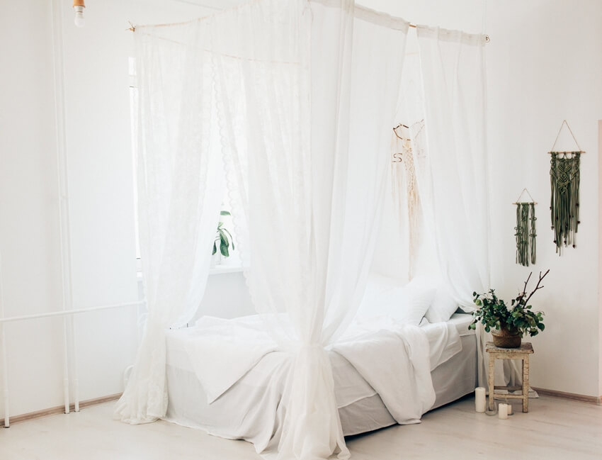 Cozy light bedroom in a minimalist Scandinavian style bedroom with ceiling mounted canopy bed, blanket, pillows, and plant on the side