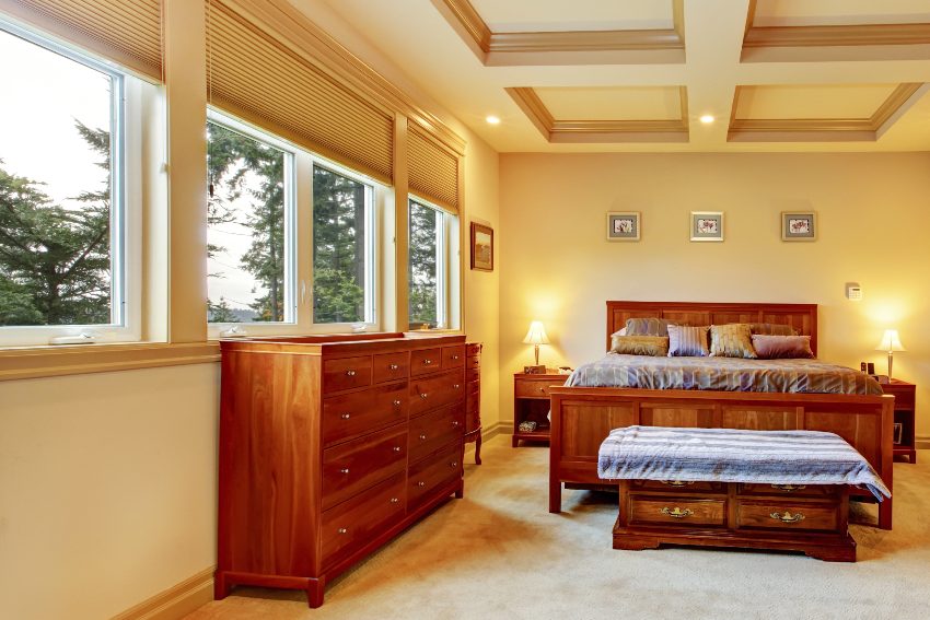 A cream color bedroom with wooden bed, vanity cabinet, trimmed ceiling, and carpet flooring