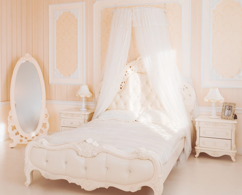 Cream white bedroom with half canopy above the bed, side tables with lamps and a standing mirror