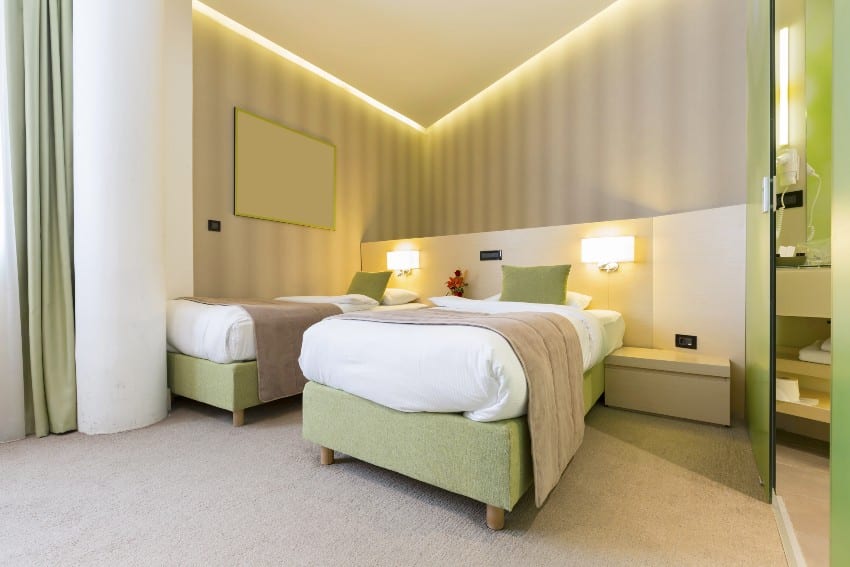 Cream with lime green tone bedroom interior features warm lighting, two single beds, and carpet flooring