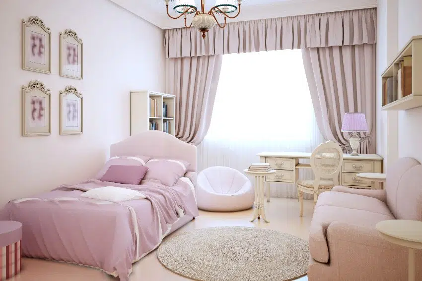 Cute pink girl's room with cream color walls, large bed with pillows and blanket, dressing table, and frameless armchair