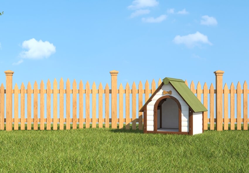 A dog's house on grass in the garden with wooden fence and blue sky