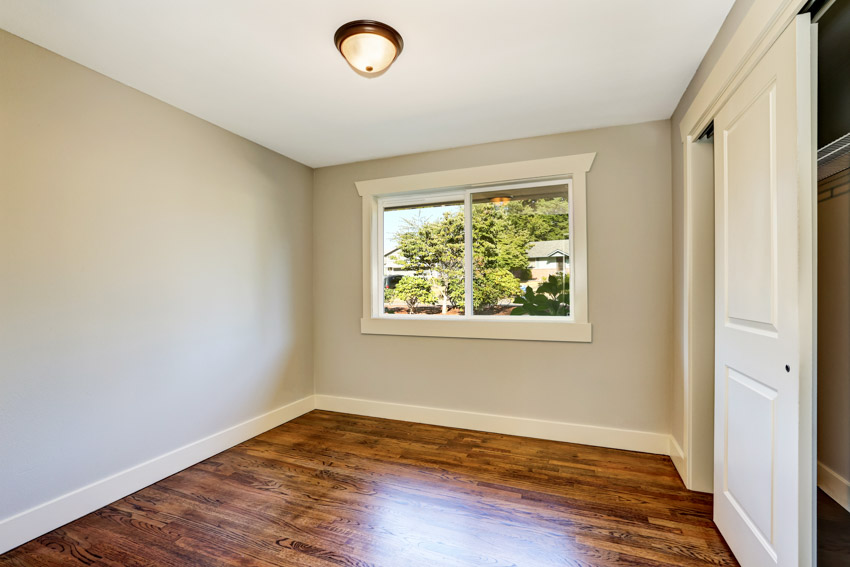 Empty room with natural Tigerwood flooring, ceiling light, door, and window