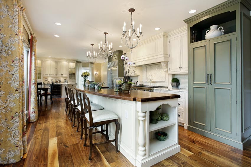 French country kitchen with chandeliers, island, countertop, chairs, range hood, cabinets, and wood flooring