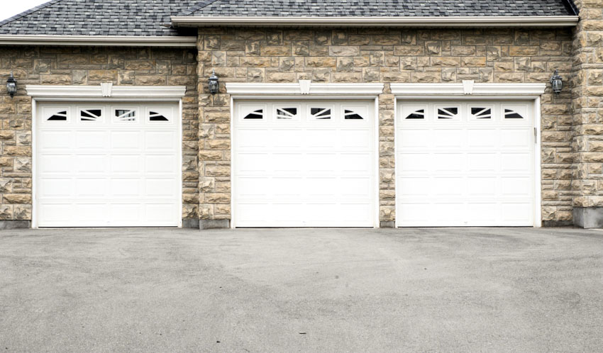 View of a garage with three doors, composite siding and driveway