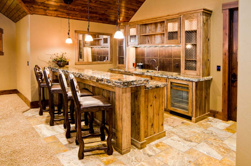 Home bar with high chairs, cabinets, bar counter, tile flooring, and pendant lighting