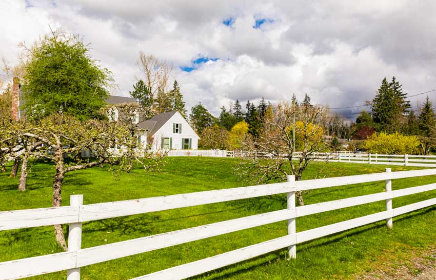 House exterior area with white split rail fence, open grass field, and trees
