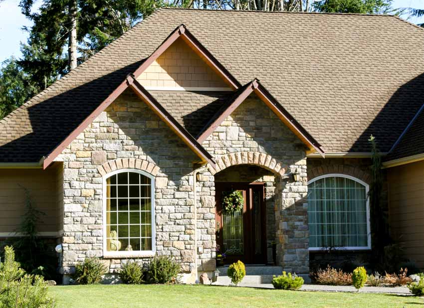 House exterior with exterior stone siding, windows, front door, and hedge plants