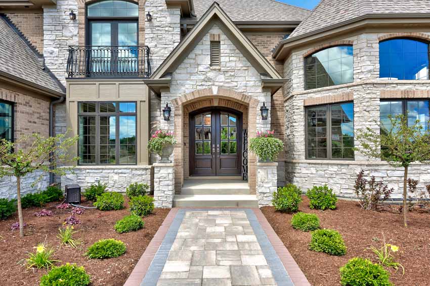 House exterior with granite stone siding, walkway, lawn plants, trees, windows, and front door