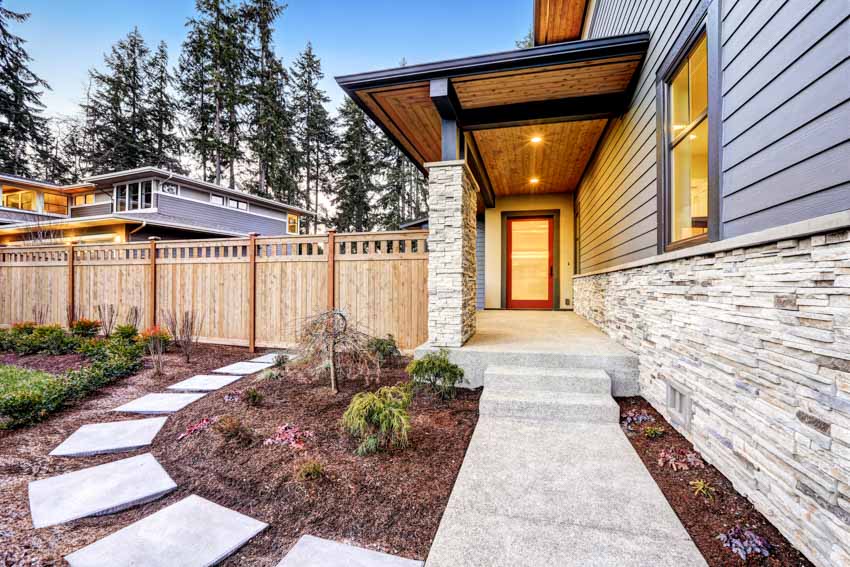 House exterior with polyurethane foam panel stone siding, walkway, door, and wooden fence