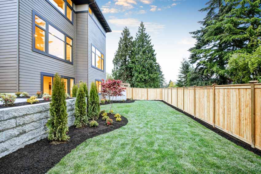 House exterior with pressure treated fence panels, siding, grass, windows, and hedge plants