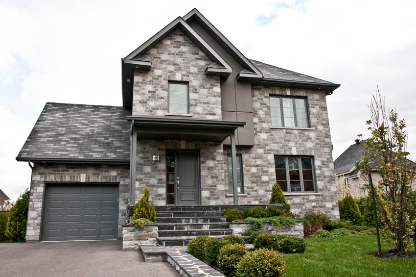 House exterior with slate stone siding, pitched roof, garage driveway, front door, windows, and lawn