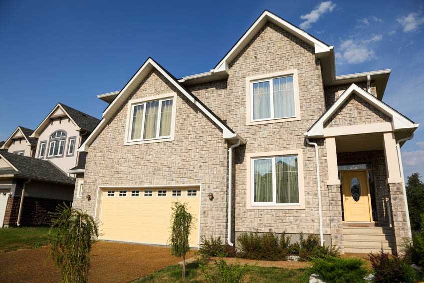 House exterior with vinyl stone siding, windows, garage door, driveway, front porch, and door