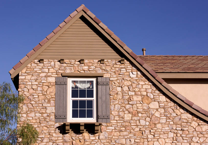 A view of a window with attached shutters on both side and cultured stone tile siding