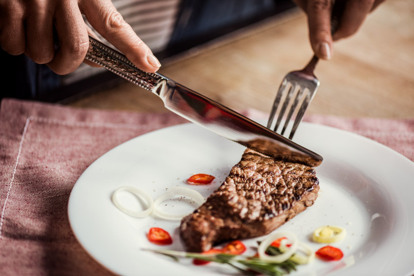 Individual cutting a steak using a silver steak knife and fork