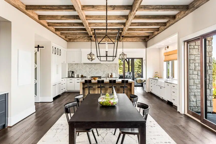 Kitchen and dining room combined with table, chairs, ceiling beams, backsplash, windows, glass door, and white cabinets