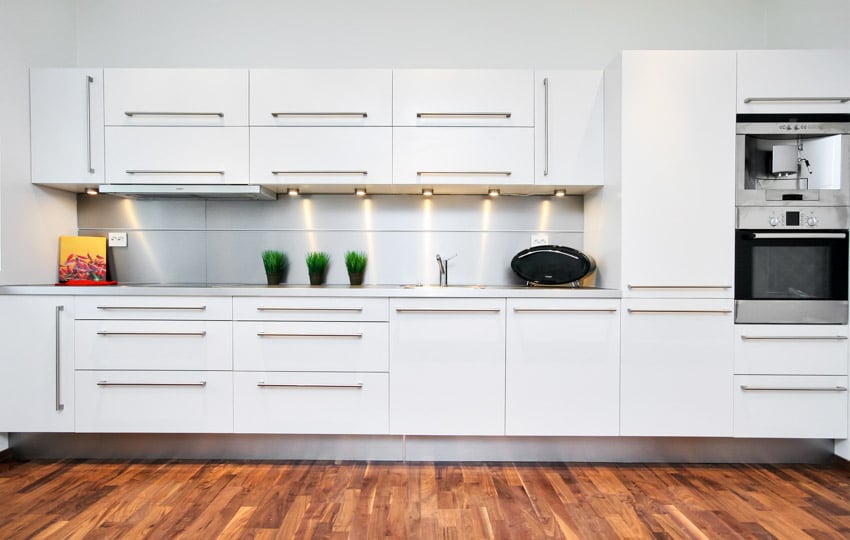 Kitchen with cabinet hardware, wood flooring, white cabinets, and backsplash