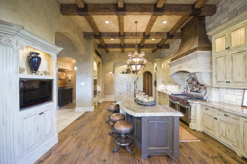 Kitchen with ceiling beams, wood floors, island, countertops, stools, cabinets, chandelier, backsplash, and stove
