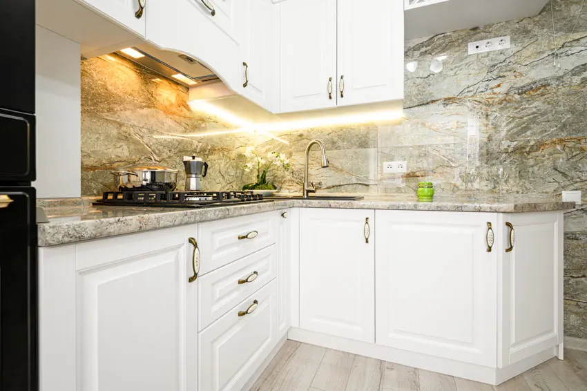 Kitchen with countertop, stone backsplash, white cabinets, and lighting fixtures