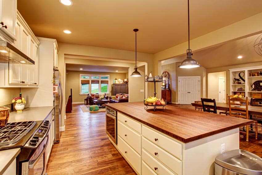 Kitchen with cedar countertops, drawers, cabinets, pendant lighting, microwave in island, and wood floors