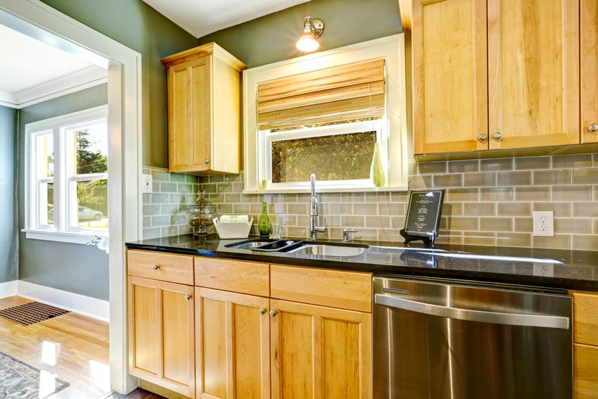 Kitchen with glass tile backsplash, maple cabinets, countertops, and roman shades