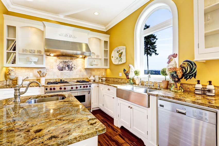 Kitchen with golden beach granite countertop, island, white cabinets, backsplash, yellow walls, sink, faucet, and window