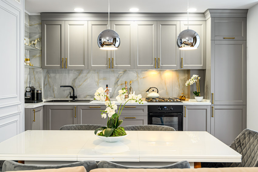 Kitchen with gray cabinets, pendant lights, table, countertops, and quartzite backsplash