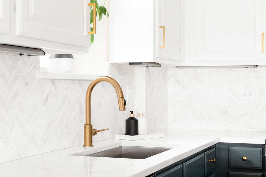 Kitchen with herringbone pattern backsplash, faucet and top cabinets with gold finish