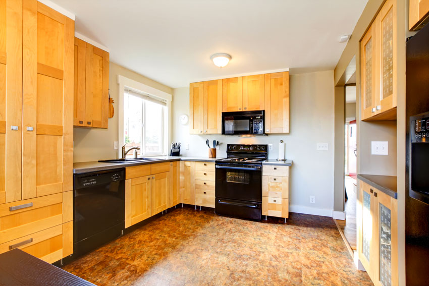 Kitchen with honey maple cabinets, resin epoxy floors, stove, oven, countertop, ceiling light, and window