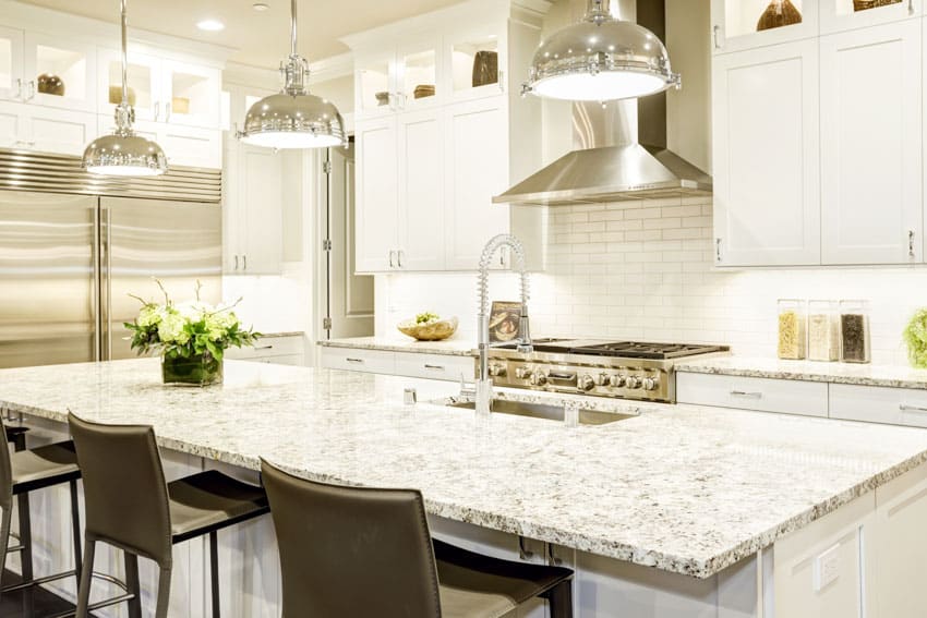 Kitchen with island, range hood, cabinets, arctic cream granite countertop, pendant lights, and chairs